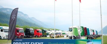 Zwanzig bunte eActros stehen vor schweizer Kulisse im Rasen