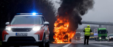 Ein brennender Lkw steht auf einer Autobahn, im Vordergrund Sicherheitskräfte