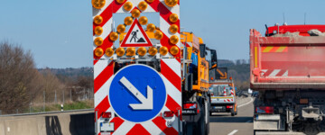 Auf der A96 führt eine Wanderbaustelle zu einspurigem Verkehr. Ein Sicherungsanhänger mit klaren Anweisungen leitet den Verkehrsfluss, um die Sicherheit auf der Autobahn zu gewährleisten