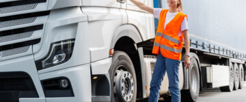 Junge Lkw-Fahrerin in Schutzkleidung an der Tür eines weißen Lkw