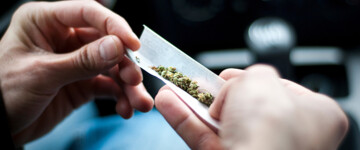 Nahaufnahme von männlichen Händen, die einen Joint im Auto drehen