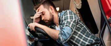 Junger Lkw-Fahrer müde oder krank über sein Lenkrad gebeugt, hält sich den Kopf