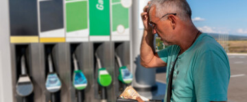Mann mit Geldbeutel staunt vor Zapfsäule über die Preise