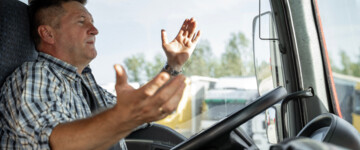 Nahaufnahme eines Lkw-Fahrers im Lkw, der angespannt und ratlos die Arme hebt