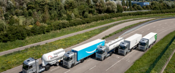 Daimler hat am 25. Juli 2024 die ersten GenH2 an Testkunden zur Probe im Praxisalltag übergeben. Die fünf Brennstoffzellen-Lkw der Testkunden fahren versetzt auf einer Straße, fotografiert von oben.