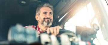 Glücklicher reifer LKW-Fahrer, der seinen LKW an einem sonnigen Tag fährt,Vorderansicht des LKW-Fahrers, der in seinem LKW sitzt