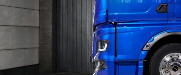 Seitenansicht des neuen MAN TGX mit seiner um 120 Millimeter nach vorne gezogenen Front. Das blau lackierte Fahrzeug steht in einer Halle