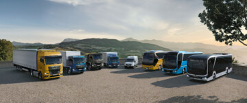 Verschiedene Nutzfahrzeuge vom Hersteller MAN Truck & Bus im Halbkreis vor hügeliger Kulisse