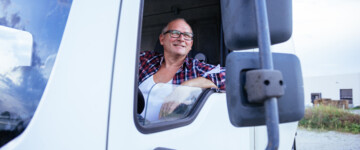 Älterer Mann oder Renter sitzt hinter dem Steuer eines Lkw und schaut lächelnd aus dem offenen Fenster in den Seitenspiegel. 