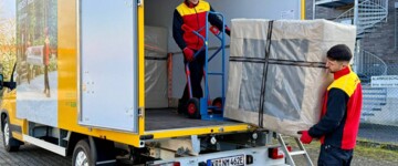Zwei Mitarbeiter von DHL 2-Mann-Handling laden ein verpacktes Möbelstück aus ihrem Transporter