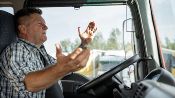 Nahaufnahme eines Lkw-Fahrers im Lkw, der angespannt und ratlos die Arme hebt