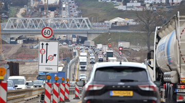 Eine Autobahnbaustelle an der A8 bei Pforzheim von Anfang 2025. Dichter Verkehr mit Autos und Lkw fließt in beide Richtungen mit gelben Fahrstreifen. Warnbaken und ein Hinweisschild mit Fahrstreifen, Grenze der Fahrzeugbreite und Tempolimit sind im Vordergrund links neben einem Auto zu sehen
