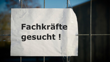 Schild "Fachkräfte gesucht" hängt an einem Gitterzaun
