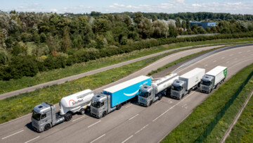 Daimler hat am 25. Juli 2024 die ersten GenH2 an Testkunden zur Probe im Praxisalltag übergeben. Die fünf Brennstoffzellen-Lkw der Testkunden fahren versetzt auf einer Straße, fotografiert von oben.