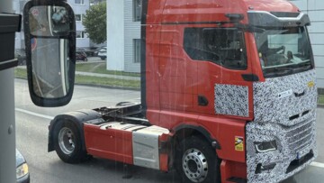 Der neue MAN TGX fährt als getarnte Sattelzugmaschine auf einer Straße. Die Front der rot lackierten Zugmaschine ist getarnt