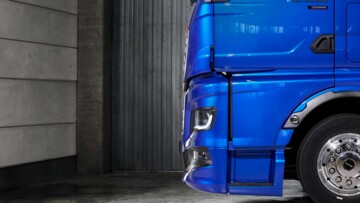 Seitenansicht des neuen MAN TGX mit seiner um 120 Millimeter nach vorne gezogenen Front. Das blau lackierte Fahrzeug steht in einer Halle