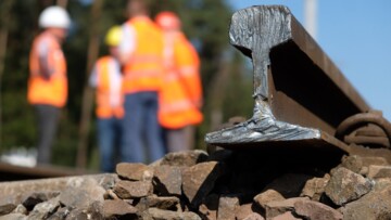 Bauarbeiter am Bahnknoten Dessau-Roßlau. Im Vordergrund als Detailaufnahme ein ins Gleisbett verlegter Schienenstrang, der noch nicht an das nächste Teilstück geschweißt wurde