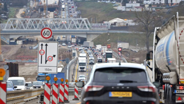 Eine Autobahnbaustelle an der A8 bei Pforzheim von Anfang 2025. Dichter Verkehr mit Autos und Lkw fließt in beide Richtungen mit gelben Fahrstreifen. Warnbaken und ein Hinweisschild mit Fahrstreifen, Grenze der Fahrzeugbreite und Tempolimit sind im Vordergrund links neben einem Auto zu sehen