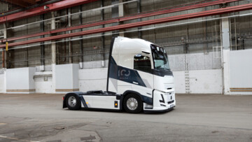 Das neue Sondermodell von Volvo Trucks steht in einer Halle. Die Solo-Sattelzugmaschine ist von vorne rechts fotografiert und präsentiert sich in weißer Lackierung mir schwarzen 100-Jahre-Jubiläums-Schriftzügen  