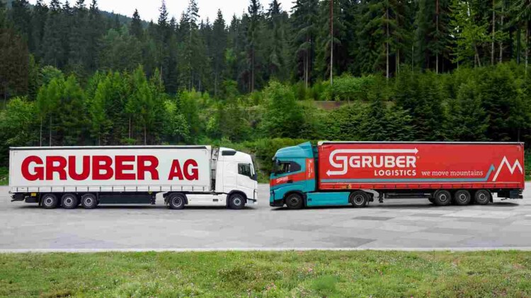 Symbolbild der Übernahme von Gruber AG durch Gruber Logistics im Jahr 2026: Zwei Lkw stehen sich auf einem Parkplatz gegenüber, Links mit Logo und CI der Gruber AG, rechts mit Logo und CI von Gruber Logistics