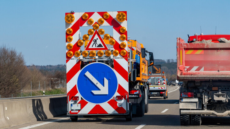 Auf der A96 führt eine Wanderbaustelle zu einspurigem Verkehr. Ein Sicherungsanhänger mit klaren Anweisungen leitet den Verkehrsfluss, um die Sicherheit auf der Autobahn zu gewährleisten