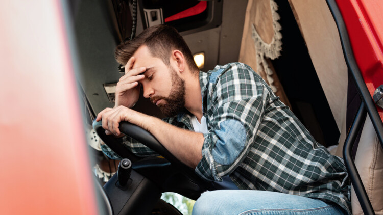 Junger Lkw-Fahrer müde oder krank über sein Lenkrad gebeugt, hält sich den Kopf