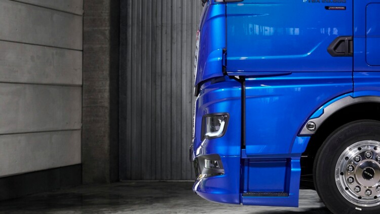 Seitenansicht des neuen MAN TGX mit seiner um 120 Millimeter nach vorne gezogenen Front. Das blau lackierte Fahrzeug steht in einer Halle