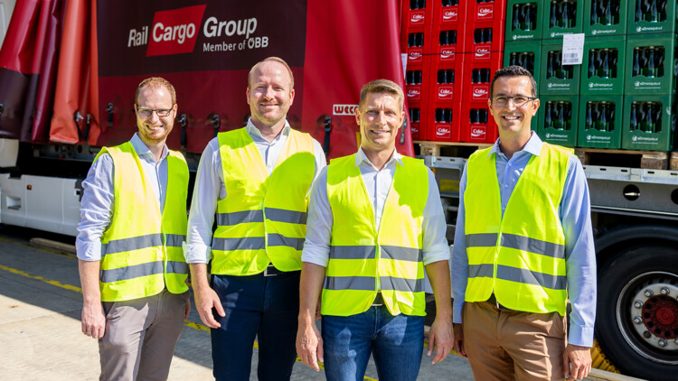 Kooperation im kombinierten Verkehr in Österreich: Gerald Leichtfried, Distribution Manager (Coca-Cola HBC Österreich), Felix Sprenger, Supply Chain Director (Coca-Cola HBC Österreich), Christoph Grasl (Vorstand RCG), Patrick Redl, Logistics Manager (Coca-Cola HBC  Österreich) stehen vor einem Trailer mit Getränkekisten, der auf einem Gleis mit einem Wagen der ÖBB-Cargotochter RCG steht