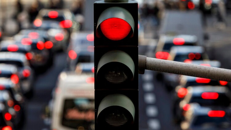 Eine rote Ampel auf der Tunisstraße in Köln zur Rush-Hour. Auf der dreispurigen Straße sind die roten Rücklichter vieler unscharfer Autos zu erkennen