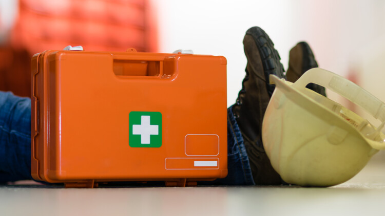 Person auf dem Boden nach Arbeitsunfall mit Verbandskasten