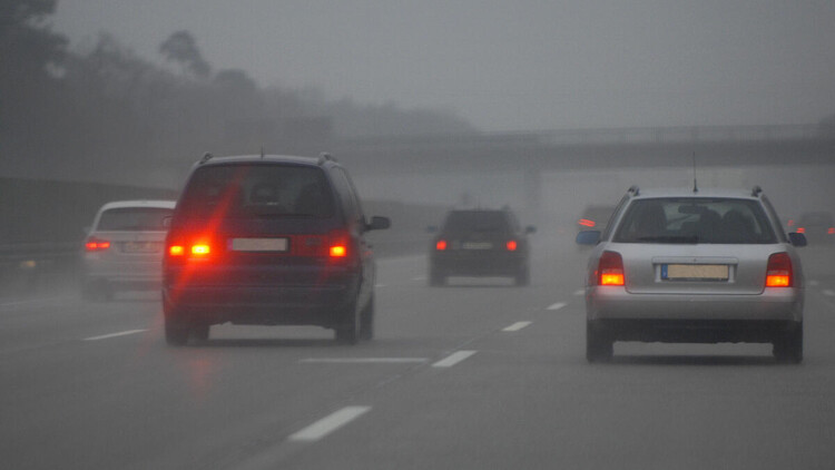 Autos fahren auf einer Autobahn mit leichtem Nebel, Rückleuchten und Nebelschlussleuchten schimmern rot