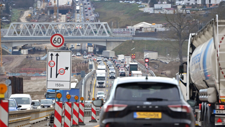 Eine Autobahnbaustelle an der A8 bei Pforzheim von Anfang 2025. Dichter Verkehr mit Autos und Lkw fließt in beide Richtungen mit gelben Fahrstreifen. Warnbaken und ein Hinweisschild mit Fahrstreifen, Grenze der Fahrzeugbreite und Tempolimit sind im Vordergrund links neben einem Auto zu sehen